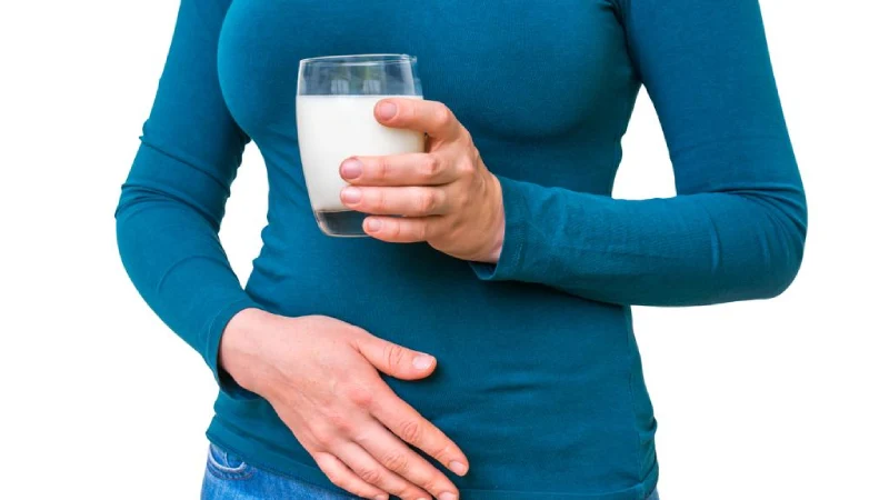 laktoz intoleransı nedeniyle karnı ağrıyan elinde süt tutan kadın